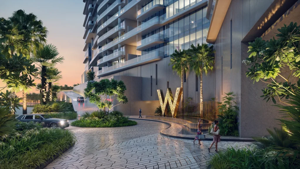 Entrada principal de W by Marriott en Al Marjan Island, con la W iluminada, palmeras y la torre de residencias al atardecer